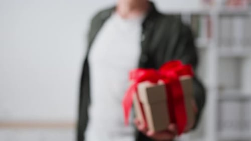 A Young Man Gives A Gift Box A Gift Close Up, Presenting A Gift Holds Out His Hand With A Gift Box