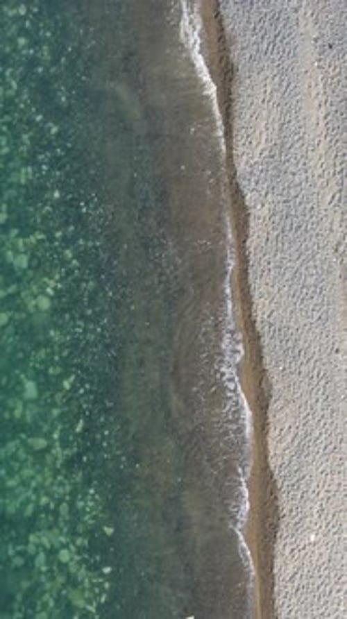 Aerial Vertical View of Beach with Wave Caressing Shore Sun Glare Small Waves on the Water Surface