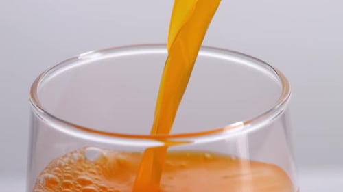 Close Up Of Orange Juice Being Poured Into A Glass On The Light White Screen Background