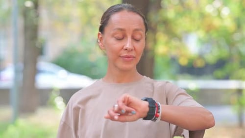 Woman Checking Watch in Urban Park on Sunny Day