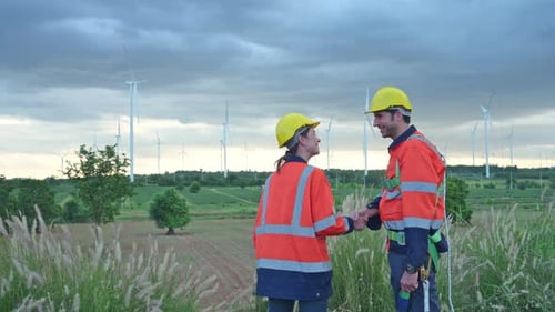 Zwei Ingenieure beim Händeschütteln vor dem Hintergrund von Windturbinen im Feld
