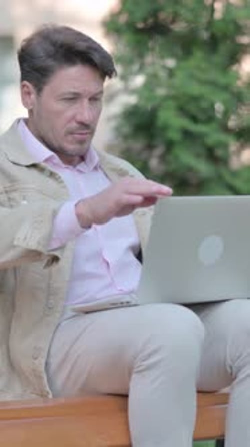 Mann geht, nachdem er den Laptop geschlossen hat, während er im Freien auf einer Bank sitzt, vertikal