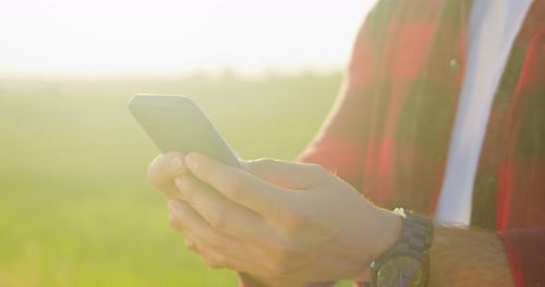 Cropped View of the Optimistic Caucasian Farmer Scientist in Plaid Shirt Using Smartphone Mobile