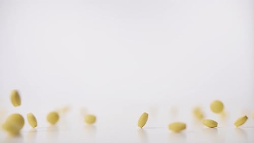 Yellow pills falling on white background in slow motion