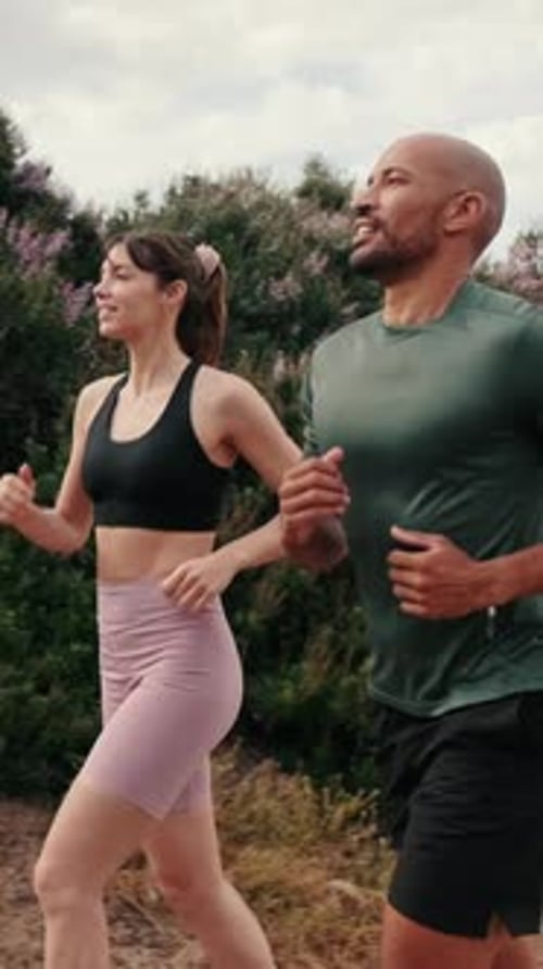 Side view of young joyful active couple jogging together in the park on summer day