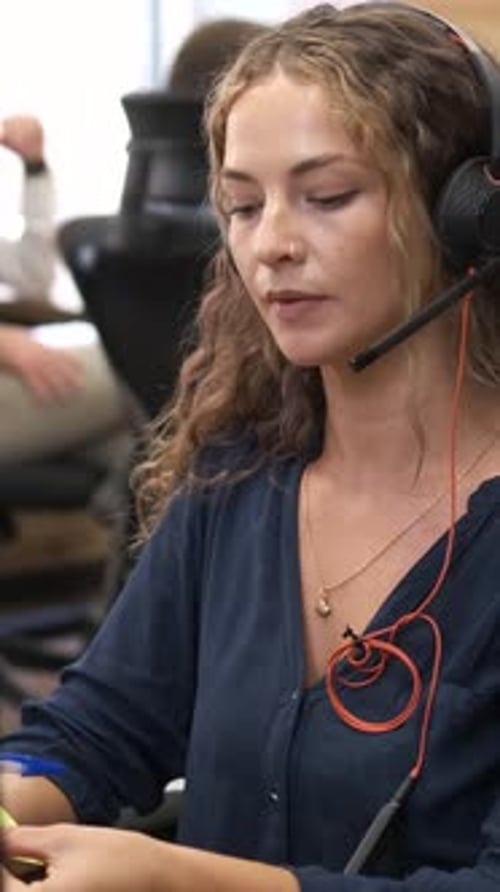 Smiling Woman Wearing Headset Takes Notes at Work