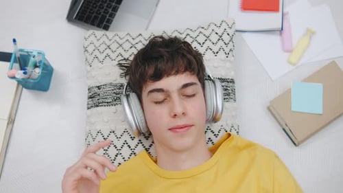 Teenager Relaxing with Headphones While Lying on a Cushion Surrounded By Study Materials and a
