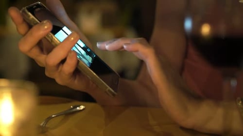 Woman Browsing Photos on Smartphone Sitting in Cafe at Night 30s