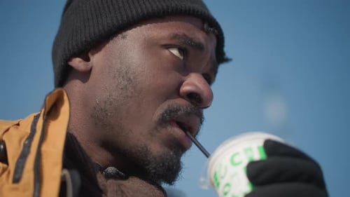 Man Drinking Drink Outside in Beanie and Jacket