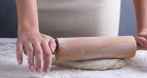 Woman shaping dough with rolling pin at white marble table against grey background, closeup