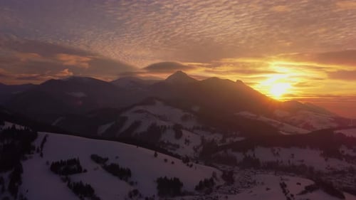 Luftbild eines Sonnenuntergangs mit orangefarbenen Wolken und ländlicher Winterlandschaft in den Bergen