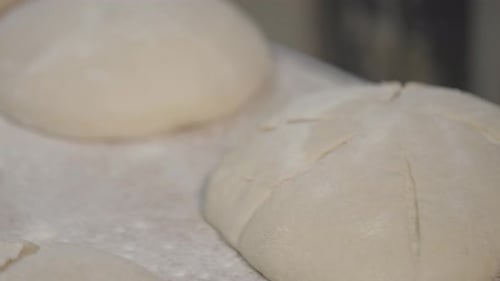 The process of making bread in a bakery. After proofing, the top of the bread is cut with knife.