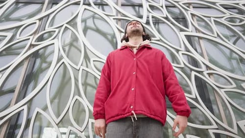 Rapper Guy in a Red Jacket Sings Rap on Street on Background Beautiful Building