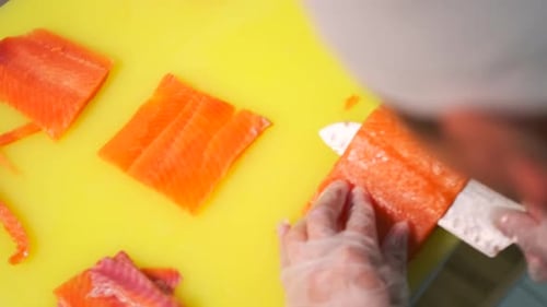 Top view, chef cuts piece of salmon steak into thin slices with sharp knife. Close up.