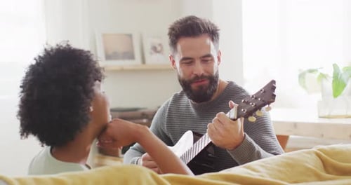 Video of rear view of happy diverse couple at home, man playing guitar, singing to woman, copy space