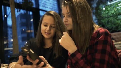 Teenage girlfriends chatting over drinks and smartphones in a trendy cafe