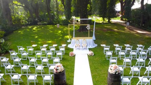 Elegant white chairs setup for outdoor wedding ceremony in lush garden