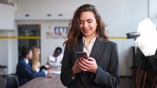 Smiling Business Woman Using Mobile Phone Typing Text Messages Standing in Office Portrait of Female