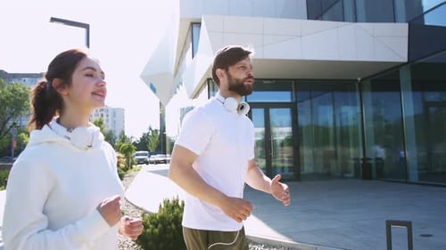 Side View of Happy Caucasian Couple with Headphones on Neck Exercising and Training on Sunny Day