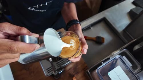 Barista making cappuccino. Barista pouring milk in cap and doing cappuccino art in coffee shop