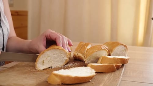 Woman slicing fresh baguette on wooden cutting board