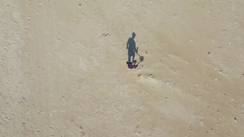 Aerial view of an unknown man using a Metal detector on a beach.