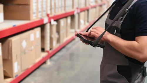 Using tablet to manage the data. Storage worker in uniform is in the warehouse