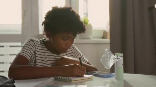 Boy Writing While Using Inhalation Mask at Home