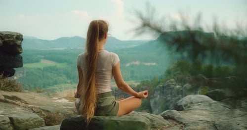 женщина медитирует на скале у реки