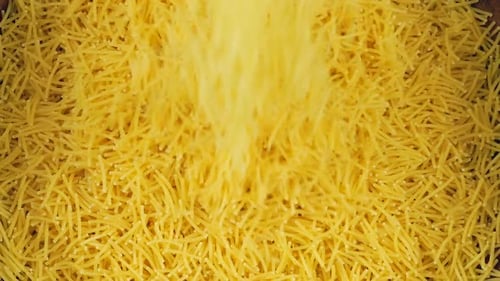 Thin small pasta is poured into a brown ceramic bowl. Top view. Slow motion.