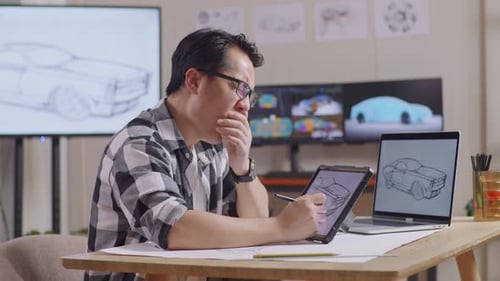 Side View Of Asian Male Yawning While Drawing New Car Design Concept On A Tablet In The Studio