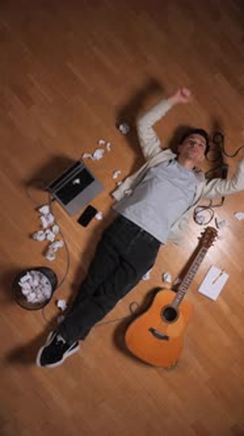 Man lies on floor with guitar and laptop