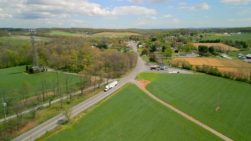 A truck backing up along a road with lush green grass during the daytime. Aerial drone view.