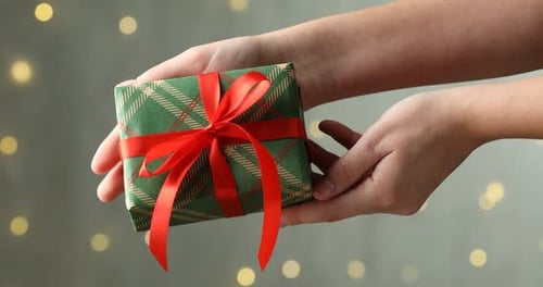 Woman holding beautiful Christmas gift box against blurred background with bokeh lights, closeup
