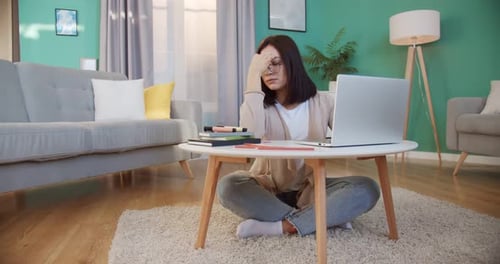 Müde von Brillen: Frau verspürt Überanstrengung der Augen, wenn sie zu Hause im Büro den Laptop benutzt, die Brille abnimmt und massiert