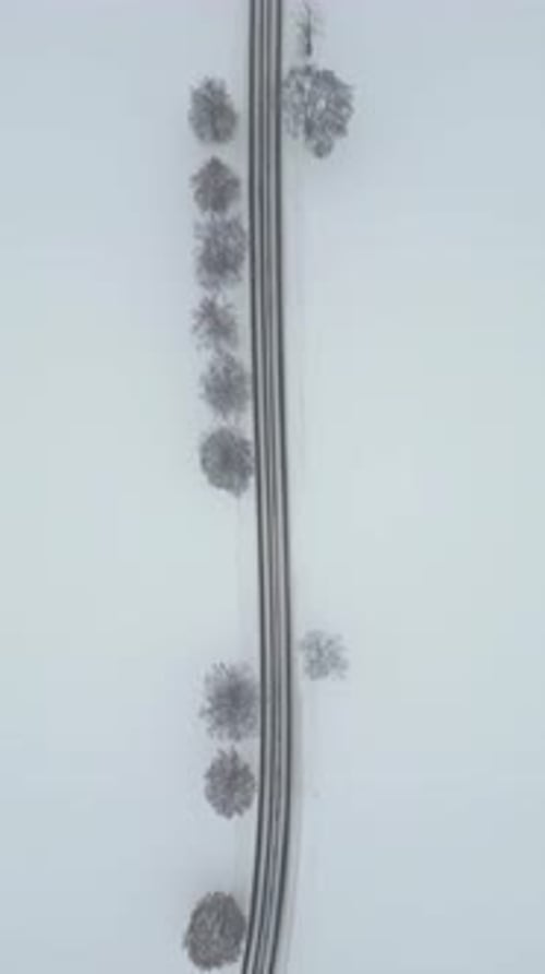 Blick von oben auf eine autofahrende Landstraße im verschneiten Winter