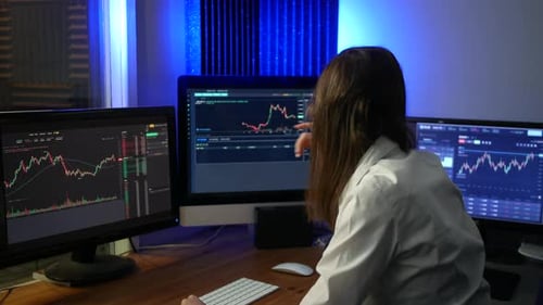 Female stock market trader analyst analysing data on computer screens comparing prices on graphs