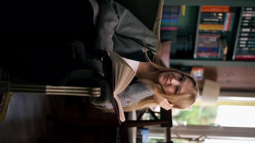 Vertical Video in a Beautiful Bookstore a Young Girl with Long Hair Sits in a Chair Reading a Book