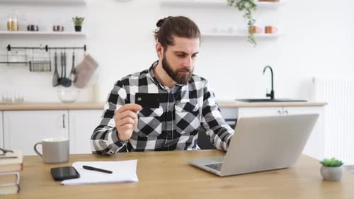 Man in Checkered Shirt Holding Credit Card While Typing on Portable Computer