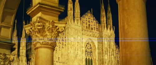 Duomo di Milano Cathedral illuminated at night from nearby archway in Italy