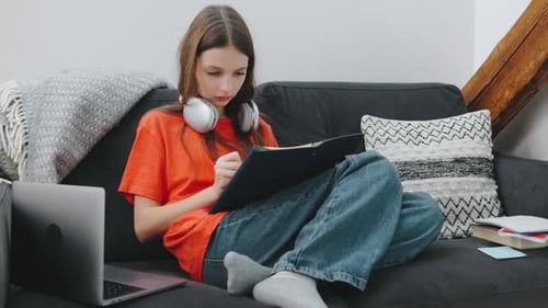 Teenager Studying on a Couch with a Laptop Notebook and Headphones in a Cozy Living Room Environment