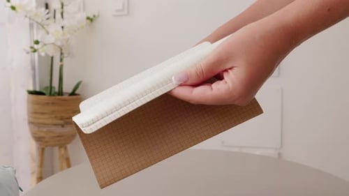 Woman Hands Opens a Grid Paper Notebook Indoors