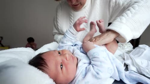 Grandmother Changes Infant Diaper, Child in Background
