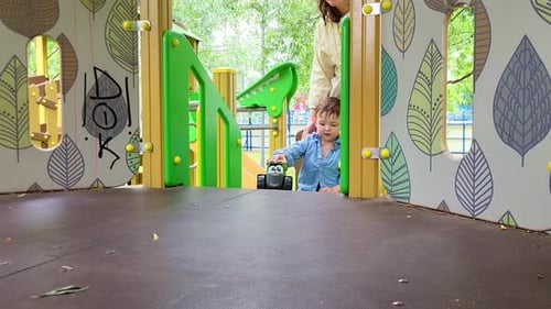 The baby with mother is having a great time on the slide at the playground. Kid boy aged two years (