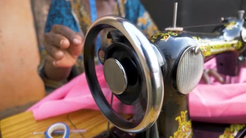 Close up shot of an African womans hands spinning the wheel on a manual operating tailoring machine.