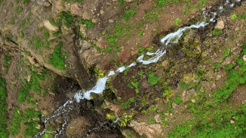 Close-Up Aerial View of Cascading Waterfall on Rocky Cliff with Greenery in Iceland