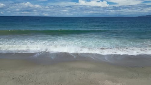 Ocean Waves on Sand Beach Against Sky with Clouds in Daytime