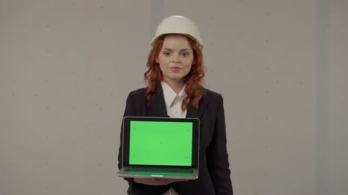 A Female Architect Holds a Laptop Screen Facing Forward Points to Its Green Screen Giving a Thumbs