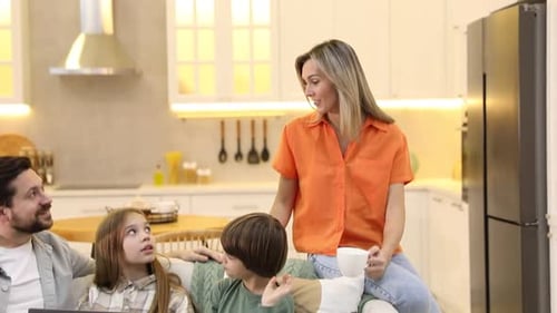 Happy family with laptop spending time together on sofa in kitchen at home. Camera moving down