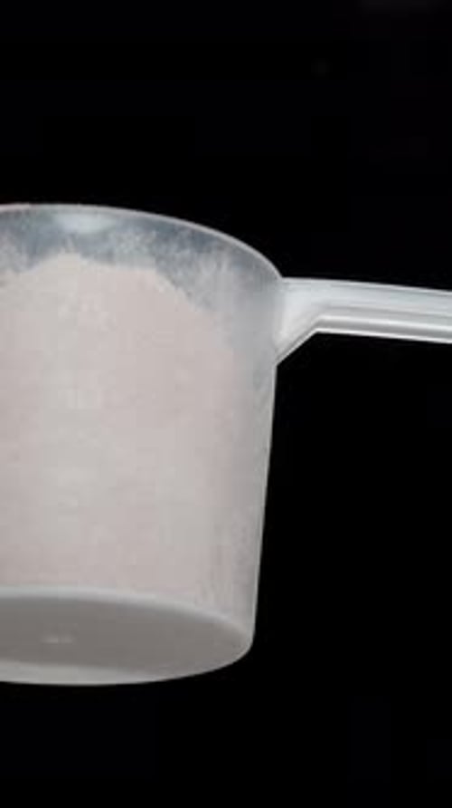 Vertical video. Top view on a black background as I sprinkle protein powder all around